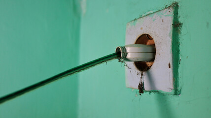 Electrical plug inserts into old wall socket in a green painted wall, showing vintage technology and potential electrical hazard.