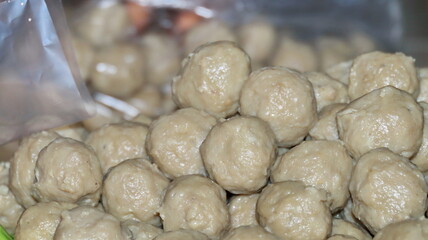 Pile of fresh meatballs sits ready for cooking in a clear plastic bag, showcasing their raw texture and inviting aroma in a culinary setting.