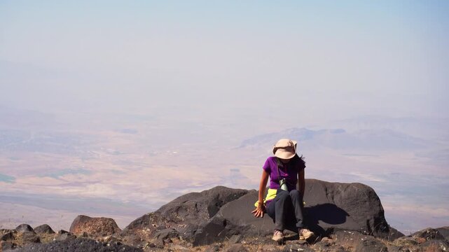 Hiker resting on rock during acclimatization process at alpine zone of Mount Ararat with wide valley views below