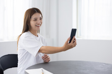 Smiling woman holding smartphone for video call or selfie at home