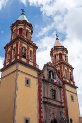Obraz premium The two tall yellow and red buildings are a church. The church has a large steeple. Historic center of Queretaro City, decorations and traditions to celebrate Mexico's Independence Day, colonial archi