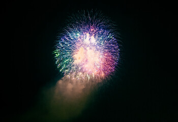 Firework sparks with smoke plumes are visible in the night sky, with colored lights and smoke forming a festive display, visible from land and water, creating a striking firework scene.