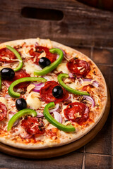 Pizza with chorizo ​​sausage, mozzarella cheese, green pepper and black olives. Rustic wooden background. Soft focus.	