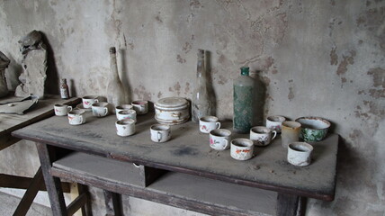 Dusty old table displays abandoned cups and bottles in a deserted room, evoking a sense of...