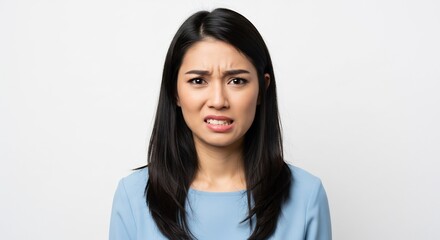 不快感や嫌悪感を露わに顔をしかめ眉をひそめる若いアジア人女性の表情がクリーンな白い背景に均一で明るいスタジオ照明で鮮明に浮かび上がる. AI Generated