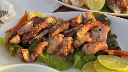 The image shows a plate of seafood with grilled shrimp, onion rings, tomato slices, and salad leaves. A lime wedge is placed in the center. A glass of drink is visible in the background.