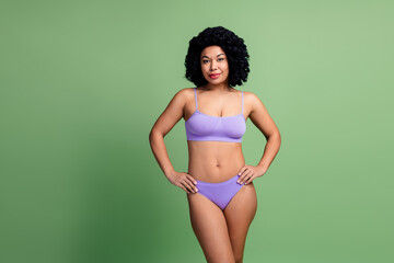 Attractive young woman in purple underwear posing against vibrant green background embodying body positivity
