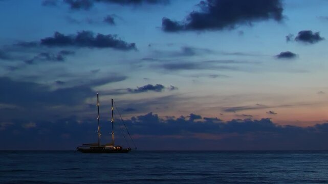 Ogliastro Marina, Italy. Blue hour video of an illuminated two-masted sailing ship anchored off Ogliastro Marina Bay, Italy, with calm Tyrrhenian waters and pastel clouds after sunset. 4K Video.