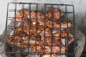 close-up shot of marinated meat grilling on a metal wire rack over an open flame or charcoal.