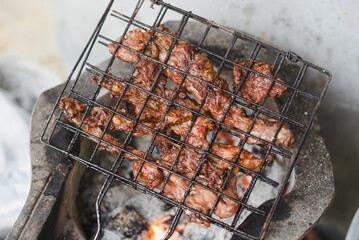close-up shot of marinated meat grilling on a metal wire rack over an open flame or charcoal.