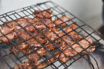 close-up shot of marinated meat grilling on a metal wire rack over an open flame or charcoal.