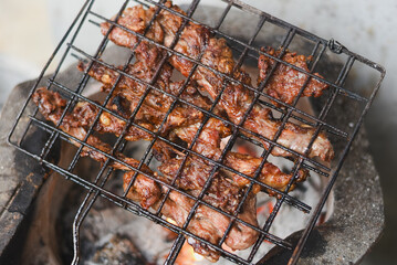 close-up shot of marinated meat grilling on a metal wire rack over an open flame or charcoal.