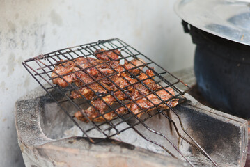 close-up shot of marinated meat grilling on a metal wire rack over an open flame or charcoal.