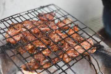 close-up shot of marinated meat grilling on a metal wire rack over an open flame or charcoal.
