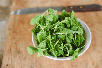 overhead shot focusing on a white bowl filled with fresh, bright green leaves placed on a light wooden surface.