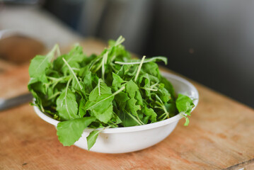 overhead shot focusing on a white bowl filled with fresh, bright green leaves placed on a light wooden surface.