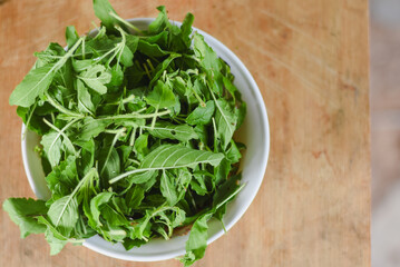 overhead shot focusing on a white bowl filled with fresh, bright green leaves placed on a light wooden surface.