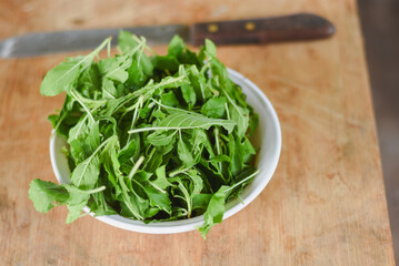 overhead shot focusing on a white bowl filled with fresh, bright green leaves placed on a light wooden surface.