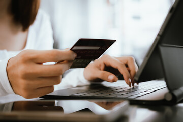 Close-up of woman holding credit card and typing on laptop, making online payment and shopping securely.