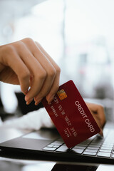 Close-up of woman holding credit card and typing on laptop, making online payment and shopping securely.