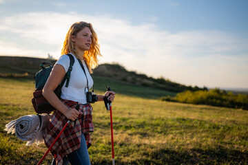 Woman hiking with backpack and trekking poles at sunset