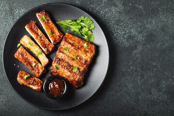 Hot grilled spare ribs from a summer BBQ served on a plate with sauce. Top view. Copy space
