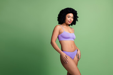 Attractive young woman in purple lingerie posing against green background celebrating body...