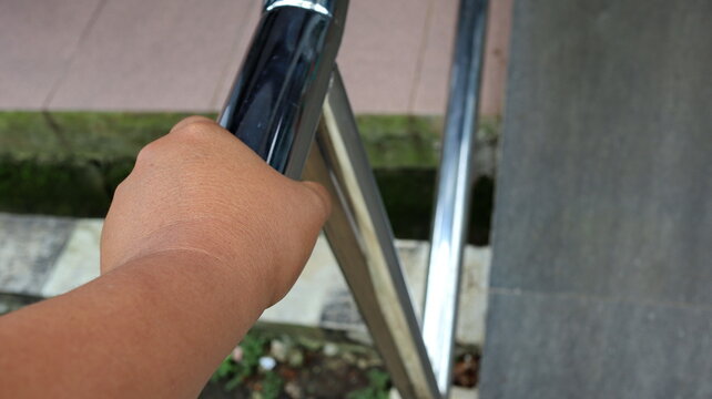 Hand grips a stainless steel railing while descending stairs outdoors, showcasing safety and accessibility in a public space on a bright day.