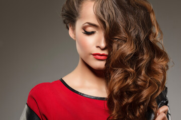 Close-up portrait of a young woman with long wavy brown hair, red lips, and perfect makeup. Fashion...
