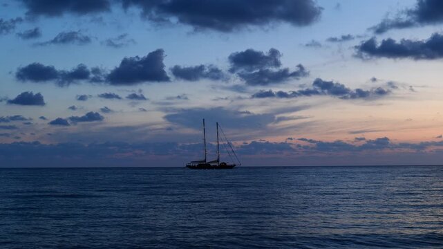 Oglaistro Marina, Italy. Blue hour seascape at Baia Arena, Ogliastro Marina Bay, Italy: calm Tyrrhenian waters and soft pastel clouds after sunset, with a two-masted sailing ship far on horizon. 4K.