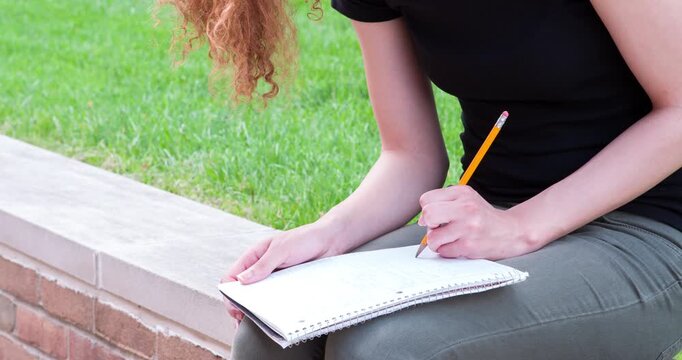 Girl outdoors writing in notebook with pencil 4k