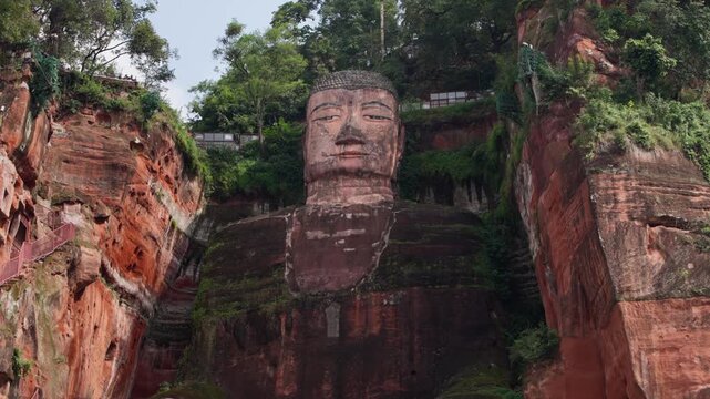 Cinematic slow motion tilt from feet to face of Leshan Giant Buddha, capturing full vertical scale and intricate cliff carving