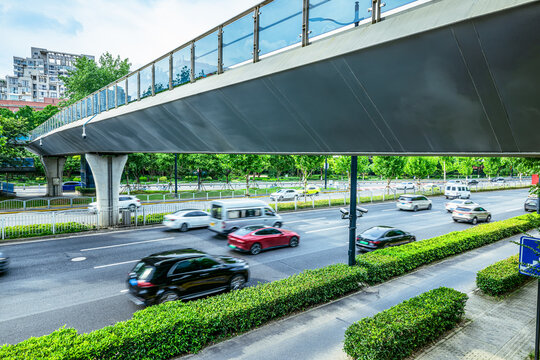 City traffic with motion blurred cars driving on a multi-lane road under a pedestrian overpass during the day.
