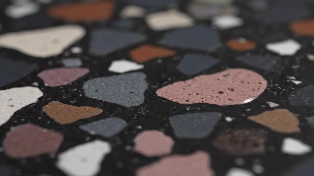 A close-up image showcasing a textured surface composed of various colored stones and aggregates embedded in a darker cement background, highlighting the intricate patterns and natural variations