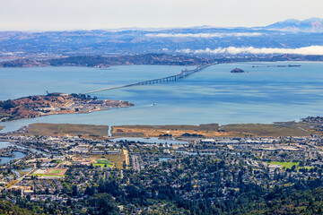 Panoramic view from Mount Tamalpais East Peak overlooking San Francisco Bay, Richmond San Rafael Bridge, Angel Island, and rolling hills of Marin County under fog and blue sky, California USA
