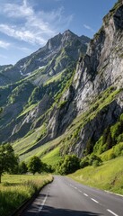 A scenic mountain road winds through a lush valley, showcasing a vibrant landscape of green hills and rugged gray rock formations under a bright blue sky.