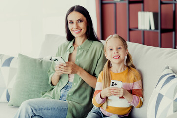 Happy mother and daughter bonding on the sofa with smartphones in a home living room environment