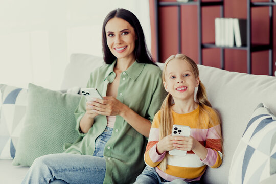 Fototapeta Happy mother and daughter bonding on the sofa with smartphones in a home living room environment