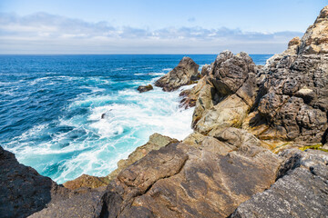 Dramatic Big Sur coastline along Highway 1, California. Waves crash against rugged cliffs, forming turquoise patterns in the Pacific Ocean, showcasing the raw beauty of the California coast