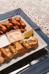 Small pieces of toasted bread and breaded cutlets with sauces served on a plate.