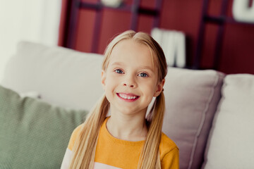 Young girl with a bright smile sitting on a cozy living room sofa in a comfortable family home...
