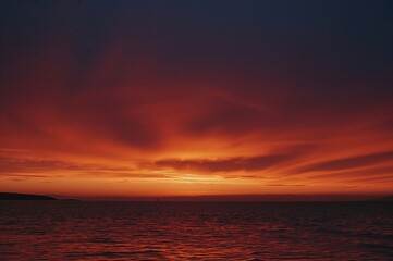 Fototapeta premium The evening sky becomes a stunning masterpiece as the sun sets, with vibrant reds, golds, and purples sweeping across the skyline, highlighted by striking silhouettes.