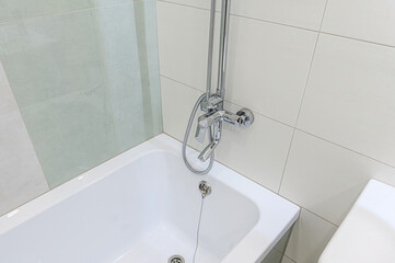 A close-up of a white bathtub with a chrome faucet and showerhead, set against tiled walls in neutral tones
