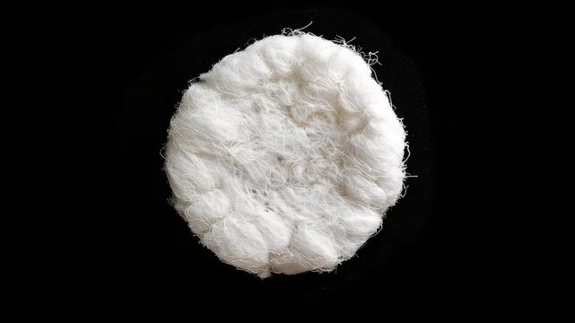 A piece of white wool sitting on a black surface, perfect for using as a texture or background