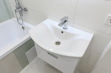 Clean bathroom corner with a white sink and chrome faucet. Tiled walls and a bathtub are also visible