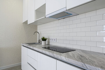 A modern kitchen features white cabinets, a gray marbled countertop, white subway tile backsplash, and stainless steel fixtures. Clean and stylish