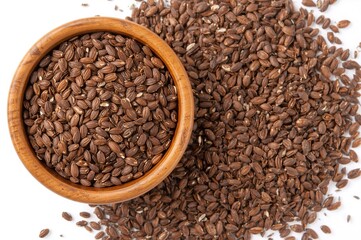 Fototapeta premium Natural wooden bowl filled with brown flax seeds with some seeds spread on a white surface