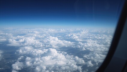 View from an aircraft window showing a high-altitude scene of the planet blanketed by fluffy white cumulus clouds