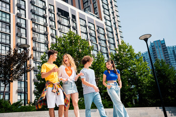 Group of cheerful young friends having fun together outdoors during sunny day near modern city architecture