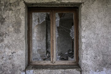 Obraz premium Derelict shattered window panes in ruined homes. Glass fragments scattered in openings. Effects of conflict and decay. Deserted, dilapidated structures. Impact of societal and economic issues.